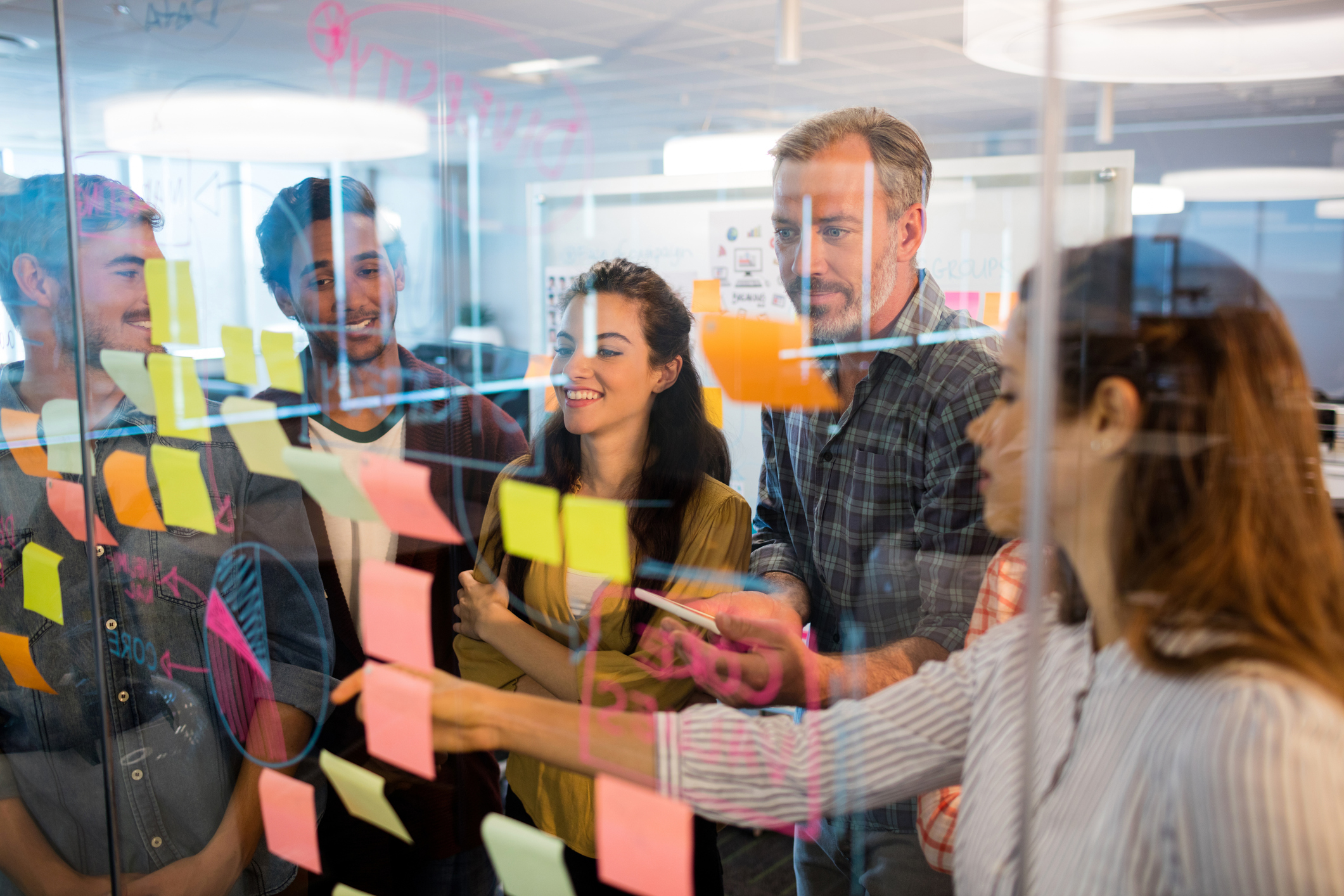 Creative business team looking at sticky notes on glass window in office