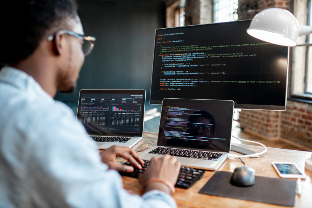 A man has code displaying on three differnet monitors, an essential skill in cloud computing