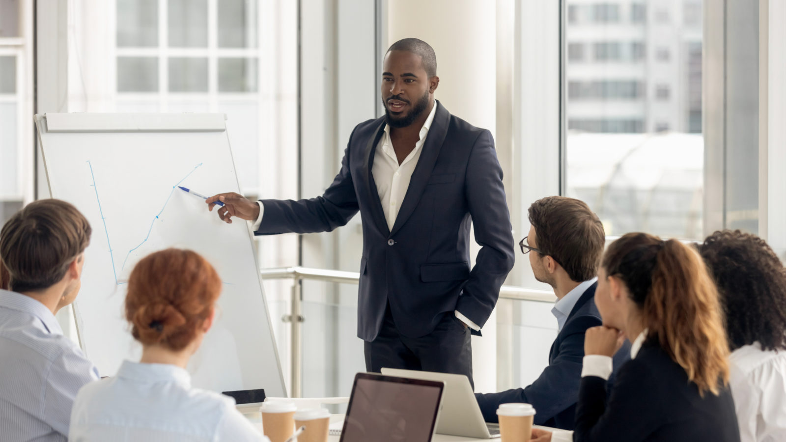 We weigh up working for startups vs working for corporations - a man stands at a board giving a presentation in a corporate office