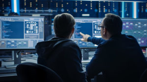 Two men sit in front of a computer screen checking cyber security, one of our 2020 trends