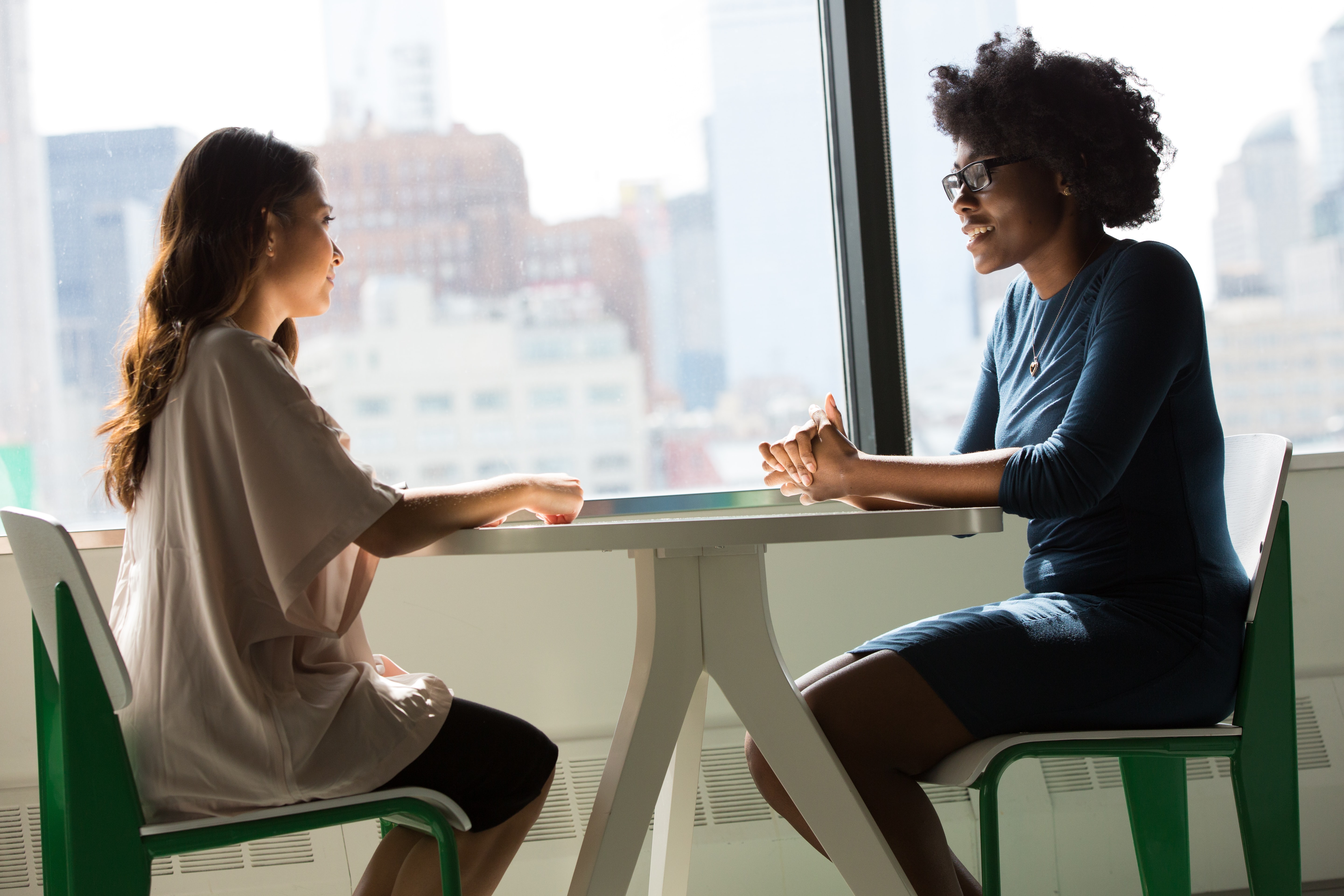 two casually dressed women sit talking across a table